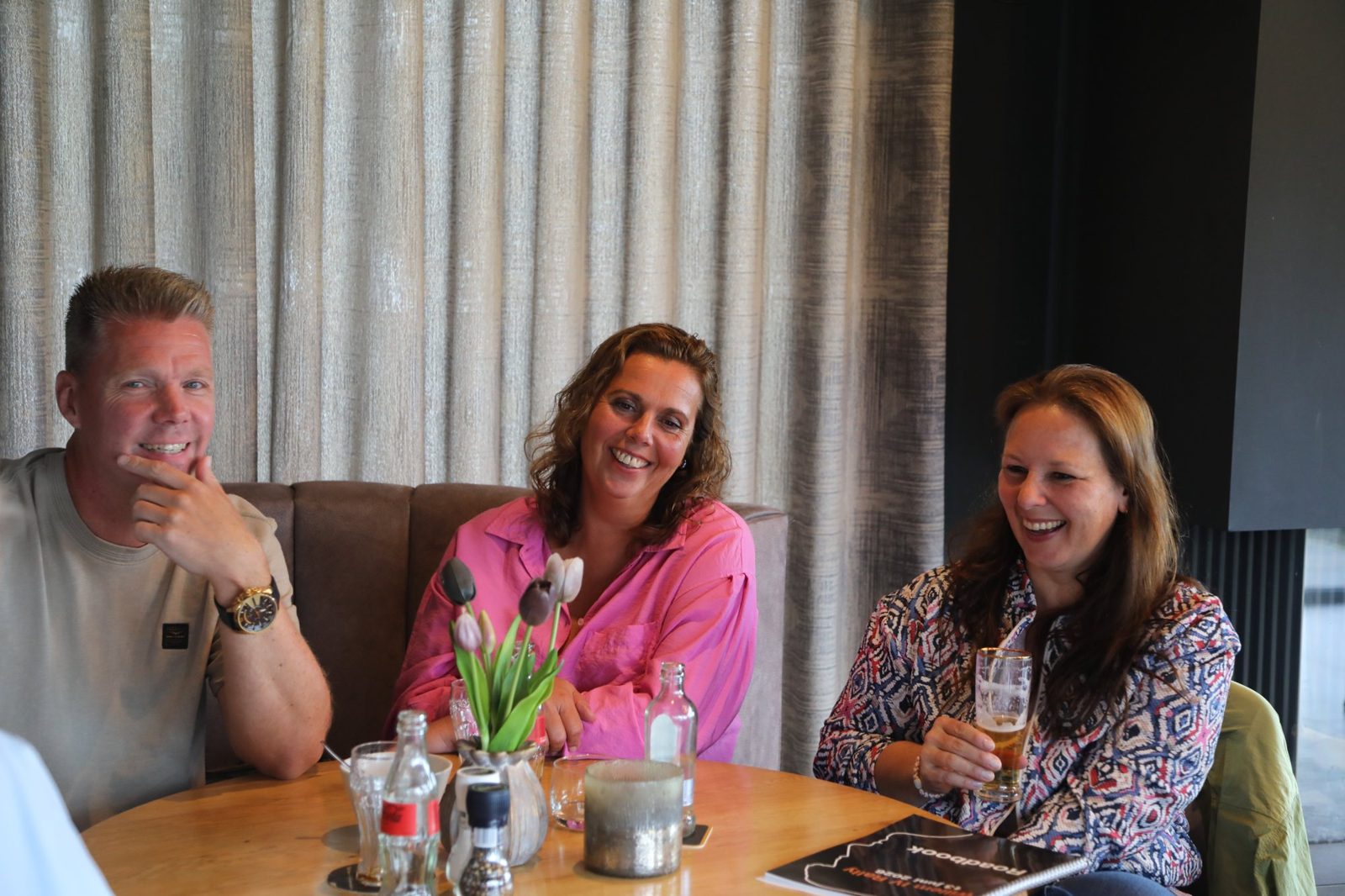 Drie deelnemers lachen samen aan tafel tijdens het diner