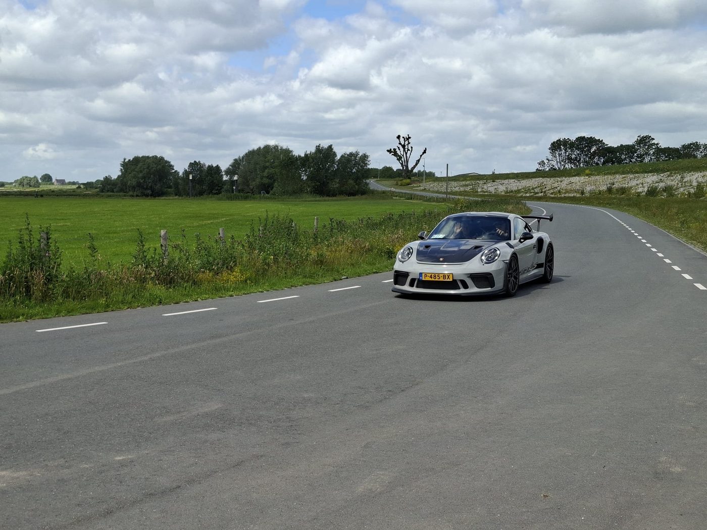 Een grijze Porsche op een dijkweggetje in de polder